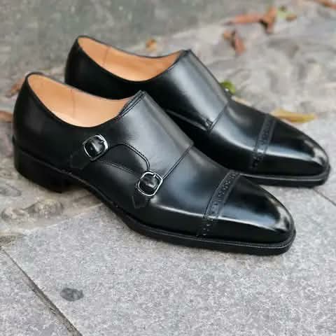 Black double monk strap shoes on stone paving.