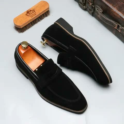 Black suede loafers with a wooden shoe brush.