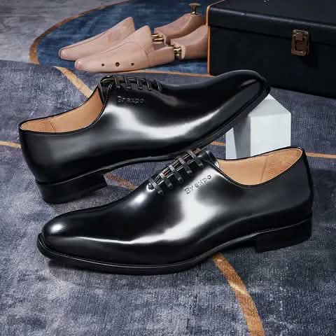 Black wholecut Oxford shoes with shoe trees and a shoebox.