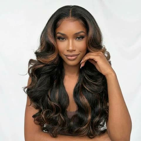 A woman wearing a dark body-wave wig with caramel highlights.