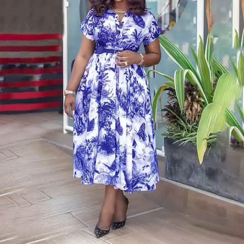 A woman wearing a blue-and-white floral print dress with short sleeves and a belt, outdoors.