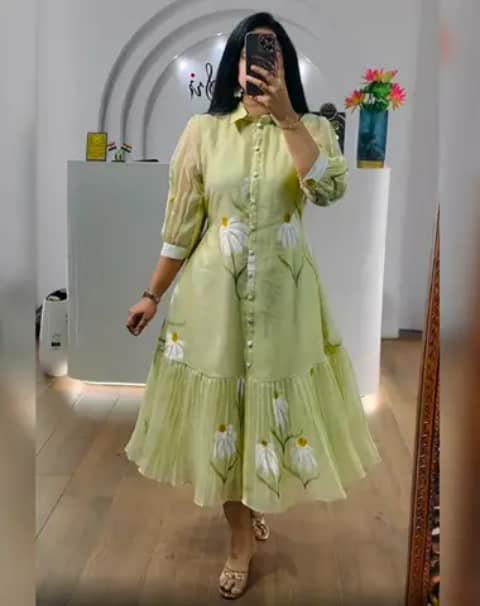 A woman taking a mirror selfie in a light-green floral shirt-style dress with a ruffled hem.