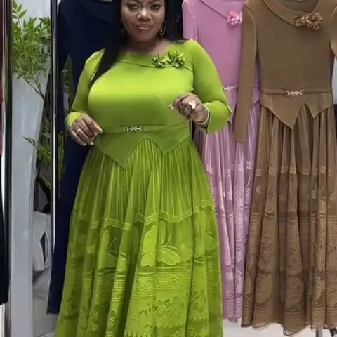 A woman wearing a long lime-green dress with a pleated skirt, with other dresses hanging behind.