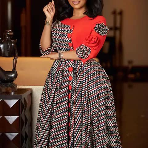 A woman wearing a long patterned dress with a red bodice, red buttons and a floral appliqué.