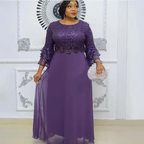 A woman wearing a long purple dress with a sequinned lace bodice and ruffled sleeves, holding a clutch.
