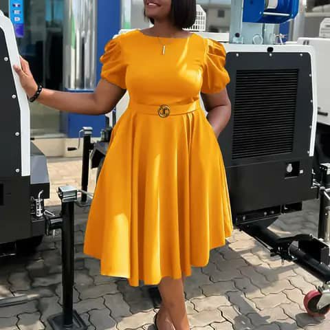 A woman wearing a mustard-yellow puff-sleeve dress with a belt, standing outdoors beside equipment.
