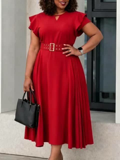 A woman wearing a red flared dress with short sleeves and a belt, holding a black handbag.