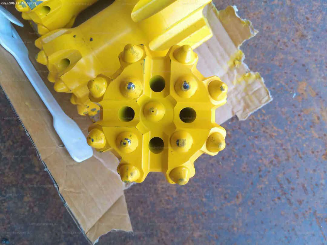 A close-up of the face of a yellow drill bit showing its buttons and holes.