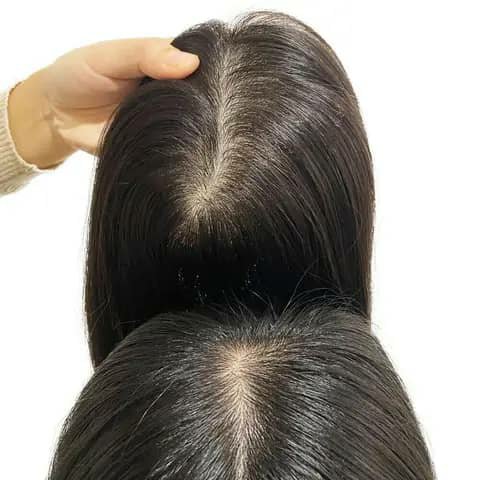 Two dark straight hair toppers shown from above, a hand holding one, showing the parting.