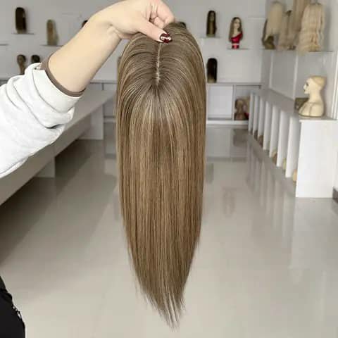 A hand holding a straight light-brown hair topper in a shop.