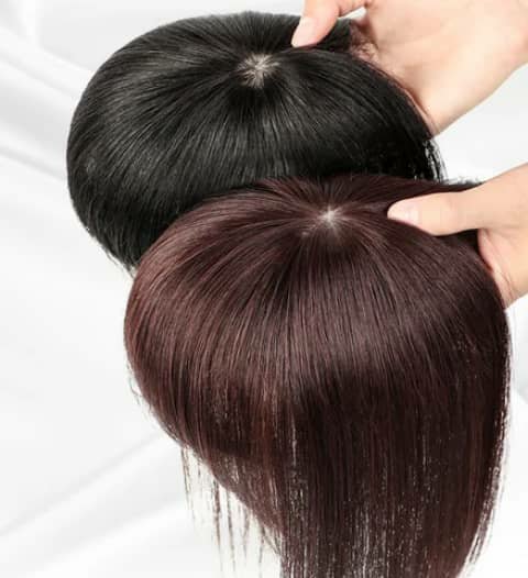 Two straight hair toppers, one black and one brown, held in hands.