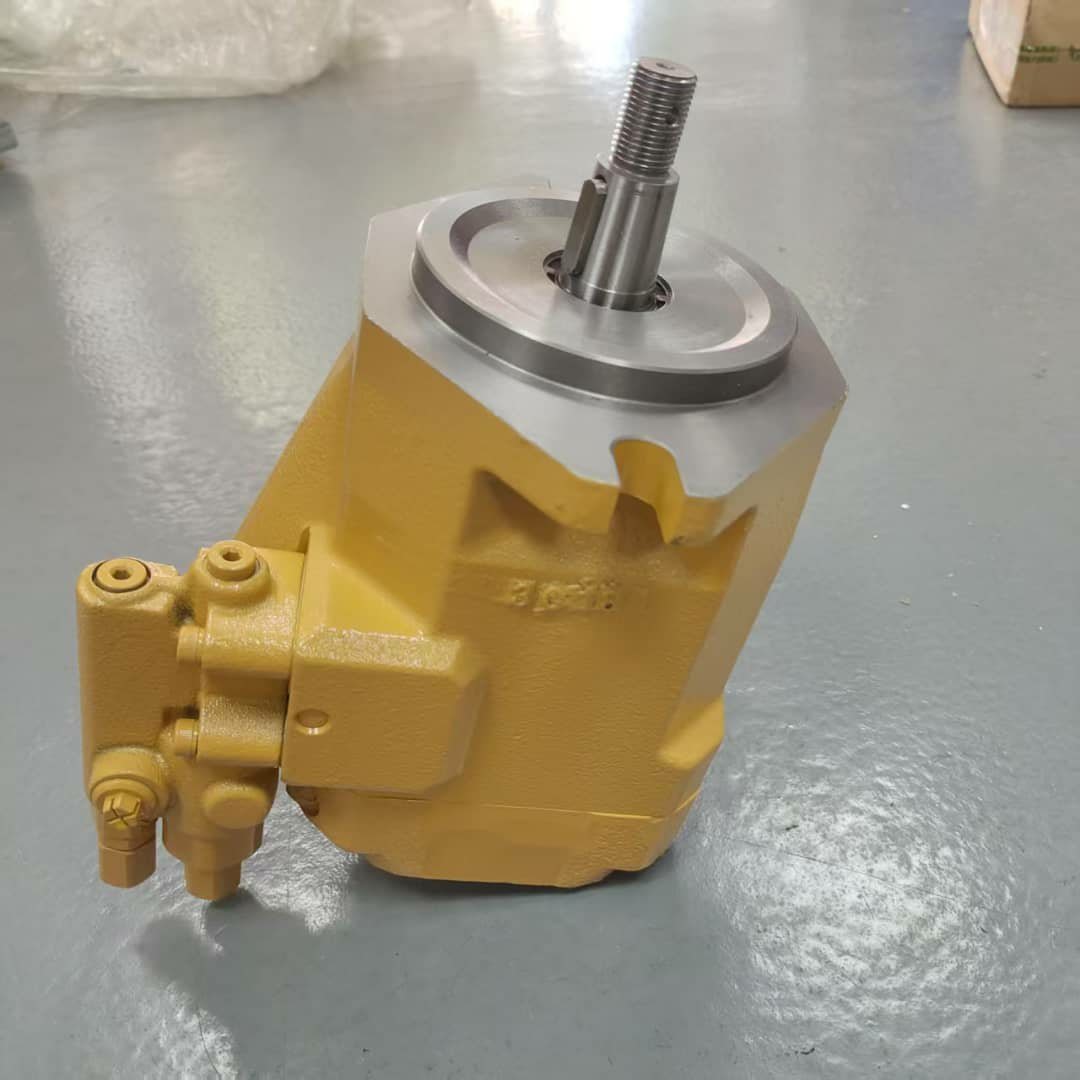 A tan hydraulic pump with a side valve block and shaft pointing up, on a grey floor.