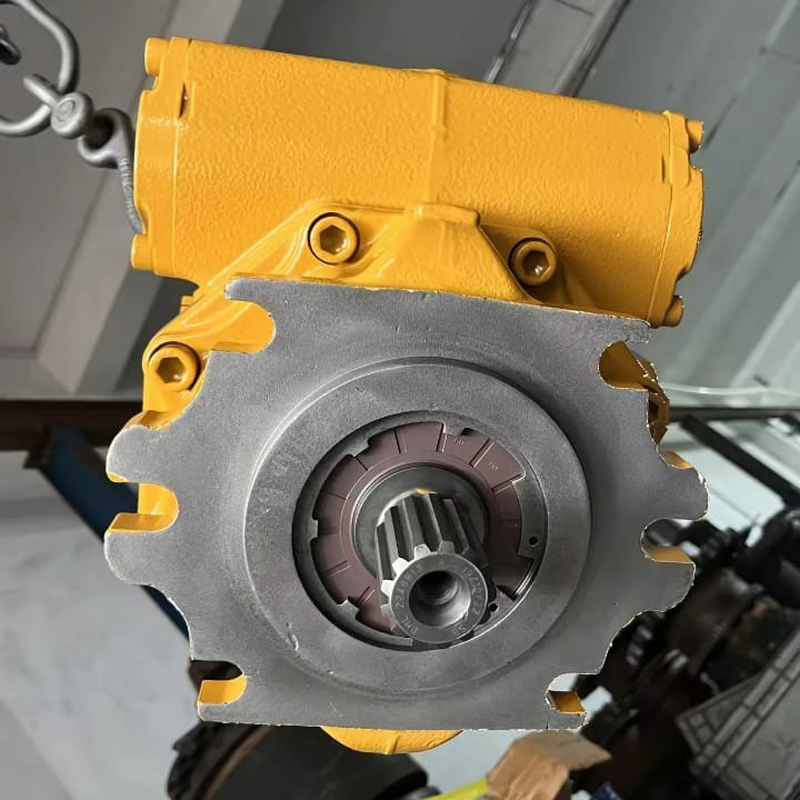 A yellow hydraulic pump with a large grey mounting flange, hanging by a hook.