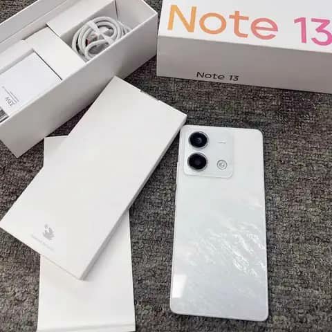 White Redmi Note 13 phone beside its box with charger