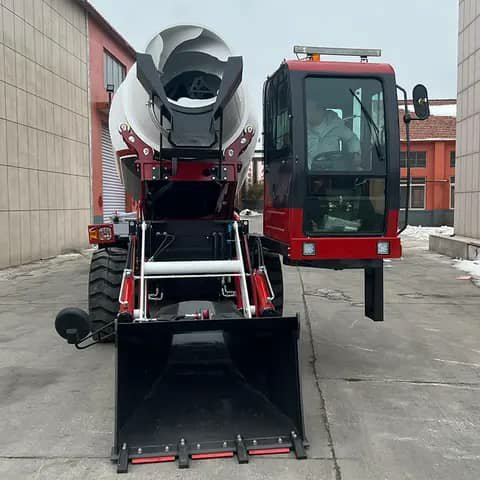 A red self-loading concrete mixer seen from the front, with its bucket lowered.