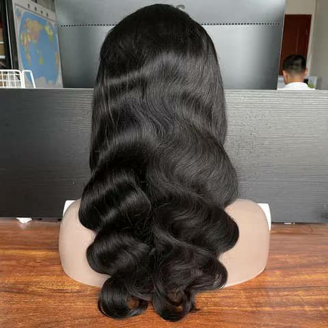 The back of a long wavy black wig on a mannequin head on a desk.