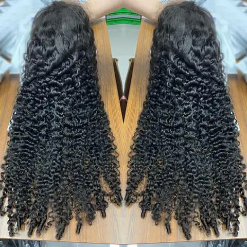 Two long dark curly wig pieces laid flat on a wooden table.