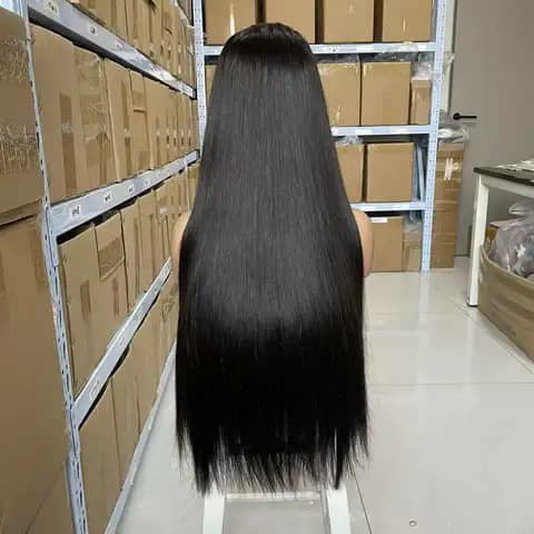 Back view of a person wearing a long straight black wig in a warehouse aisle.